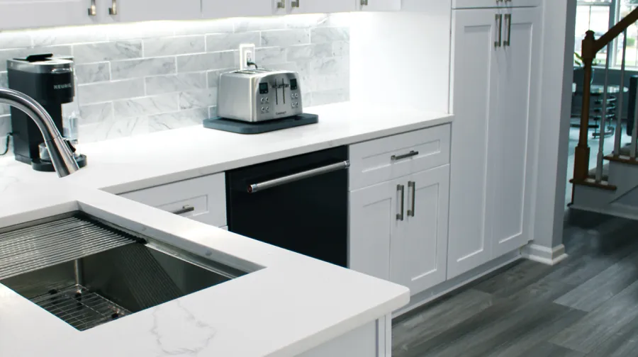 A modern kitchen with white cabinets, white quartz countertops, subway tile backsplash, and wood-look gray flooring.